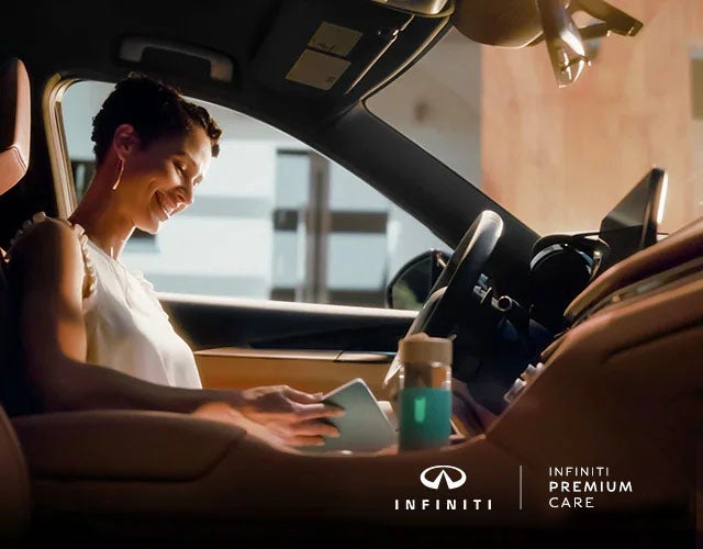 Woman sitting inside her INFINITI vehicle reading her tablet